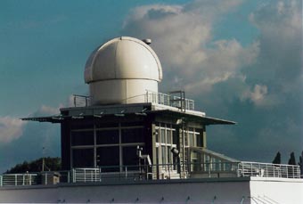 The AERONET sun photometer is located on the roof of the main building of the Institute for Tropospheric Research (IFT). In the background, the housing (white dome) of the DOAS instrument (Differential Optical Absorption Spectroscopy), that is used for horizontal aerosol and gas observations over the city of Leipzig, is shown. To the left of the DOAS housing, the green laser beam of the IFT Raman lidar is rountinely transmitted (typically twice a week). The Raman lidar measures vertical profiles of the volume extinction coefficient of the particles at 355 and 532 nm up to stratospheric heights.