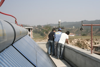 Can Li of NASA's GSFC finalizing installation and educating Prabhakar Shrestha of Duke University and a local KU student on the science and operation of the CIMEL units.  Also visible is the solar water heating units which occasionally release steam and water vapour from their fittings.