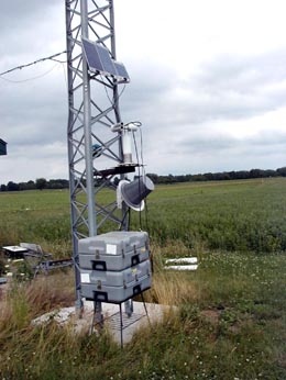 A view of the instrument mounted on an antenna tower, surrounded by cropped fields.