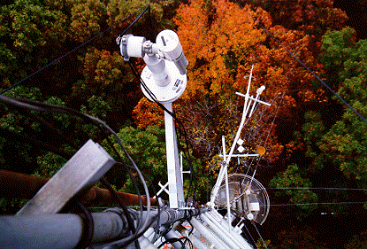 A view of the sun photometer atop a perch with glorious fall foliage in the background.